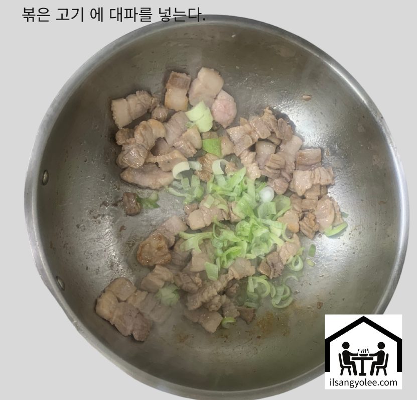 노릇하게 익어가는 돼지고기 위로 송송 썰린 대파가 추가되어 함께 볶아지고 있는 모습.