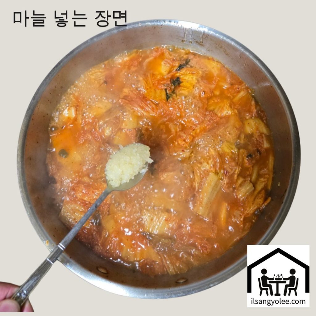 끓는 김치찌개에 다진 마늘 한 스푼을 넣는 모습