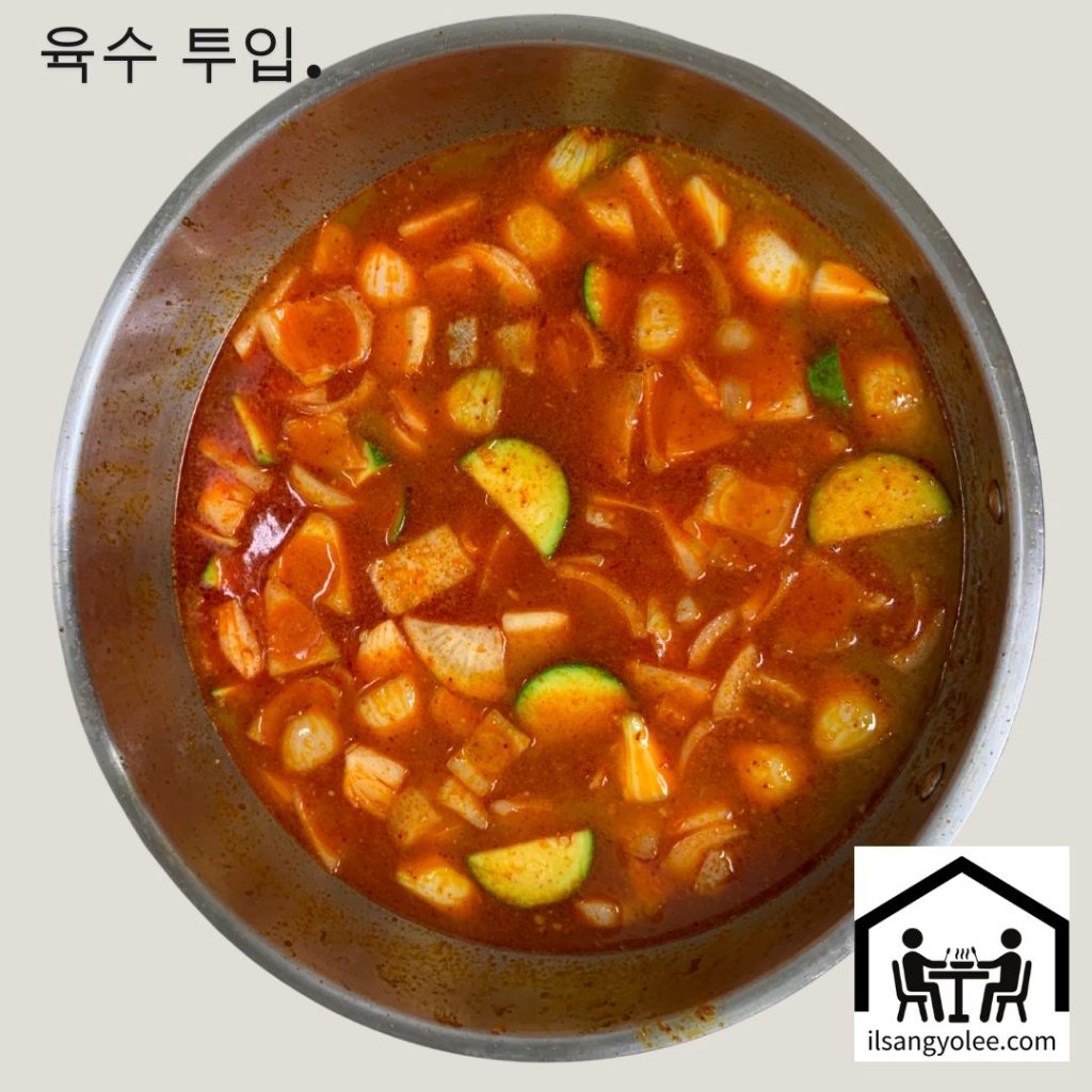 붉은색 육수가 부어진 냄비에 깍둑썰기한 양파와 애호박이 가득 담겨있는 모습